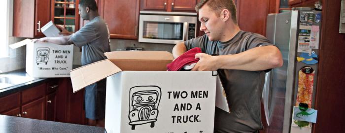 two movers packing boxes in a kitchen