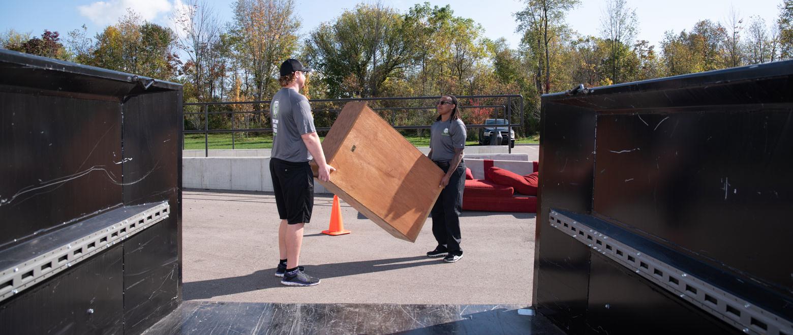 two movers carrying old furniture to a dumpster Thumbnail