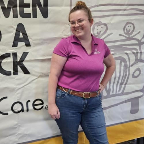 woman in purple shirt in front of business sign indoors