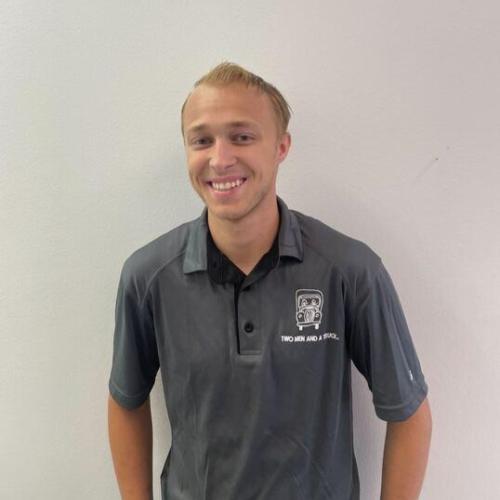Brigham is smiling in front of a gray wall