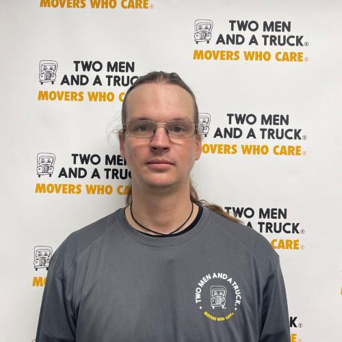 christopher jacobson standing in front of two men and a truck background wearing grey shirt