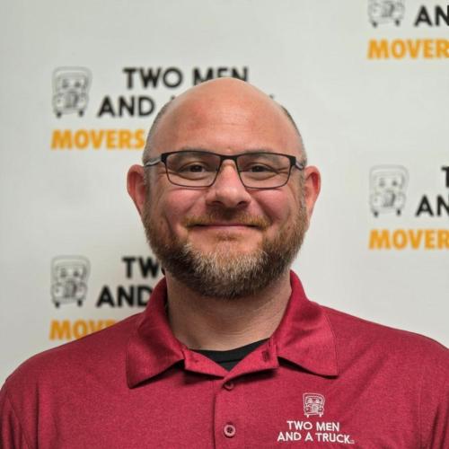 manager cody hall standing in front of two men and a truck logo background wearing red polo shirt