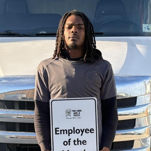 Dedrick standing in front of a moving truck holding a sign that says "Employee of the Month"