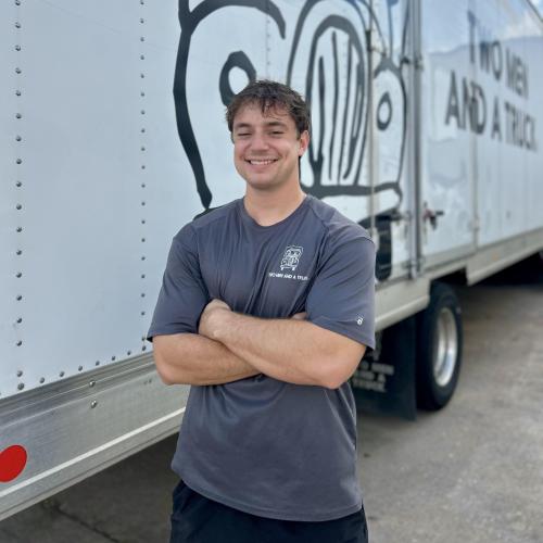 Man in front of truck with arms crossed smiling. 
