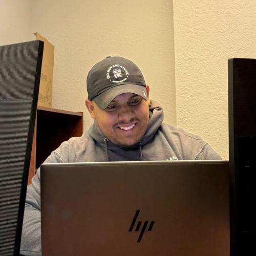 Andrew sitting at his desk behind 3 computer monitors