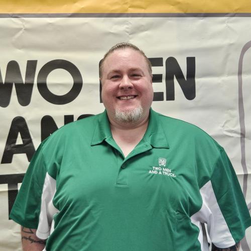 Man in green shirt in front of business sign indoors