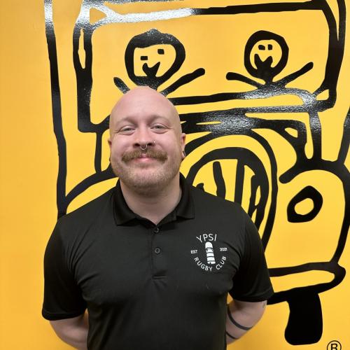 john is smiling in front of a yellow wall