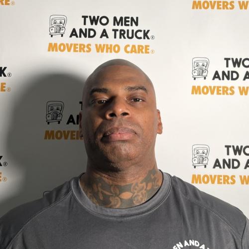 driver lionel wheeler wearing grey shirt standing in front of two men and a truck logo background