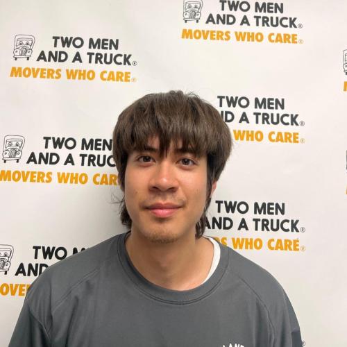 nicholas nguyen standing in front of two men and a truck background wearing grey shirt