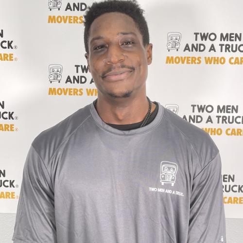 driver lionel wheeler standing in front of two men and a truck logo background wearing grey shirt