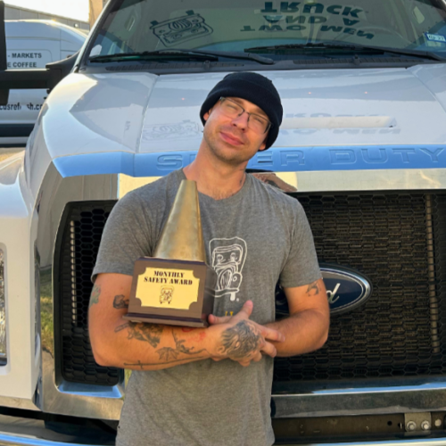 Ros standing in front of a truck holding a Safest Driver award 