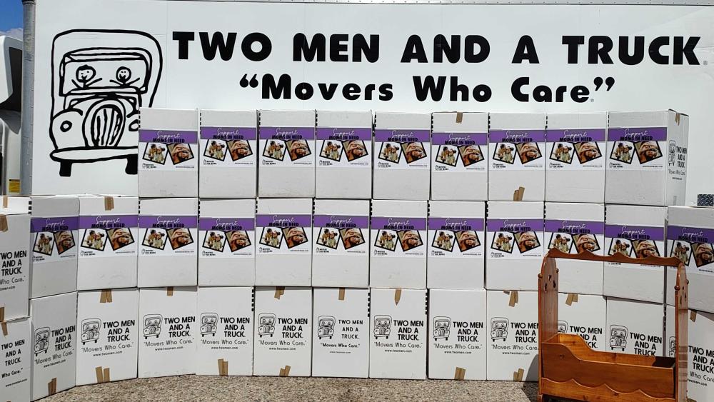 two men and a truck boxes stacked in front of a moving truck to show the amount of donations received