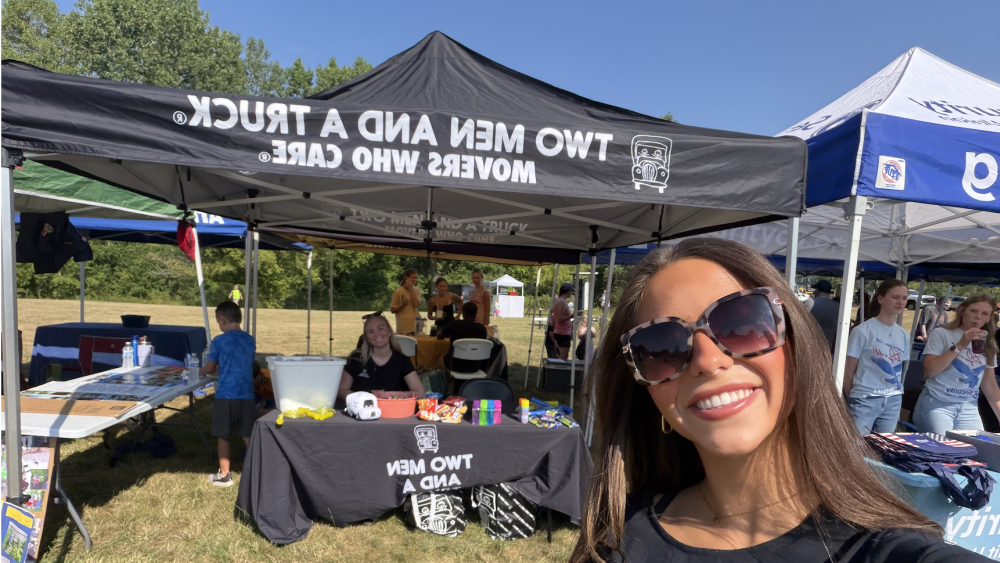 two girls at a tent and table with the two men and a truck logo.