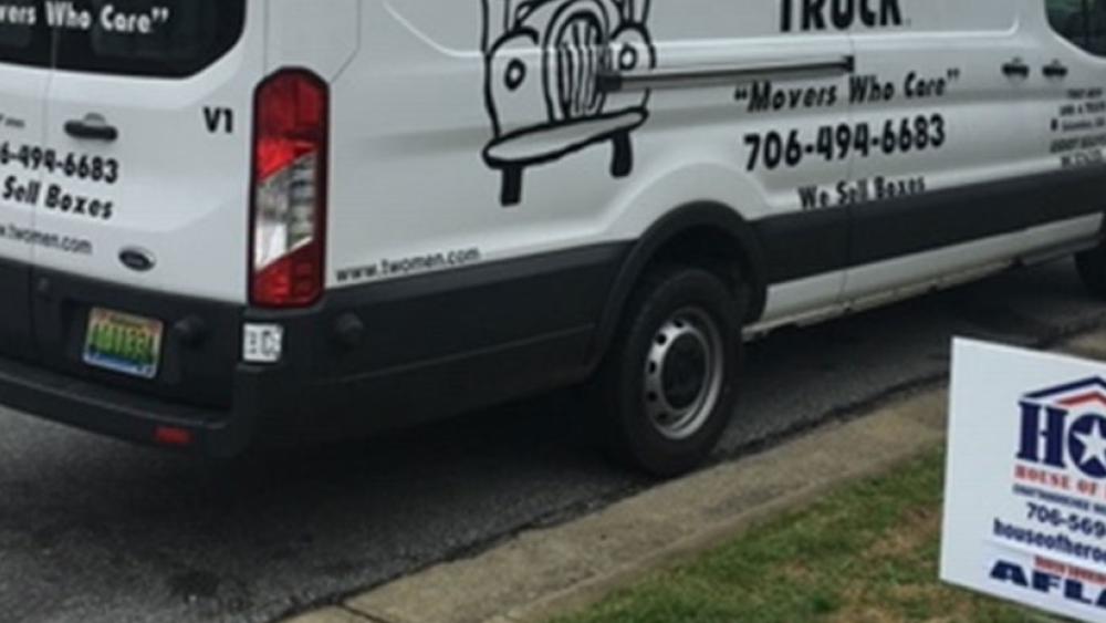 two men and a truck van with an House of heroes yard sign
