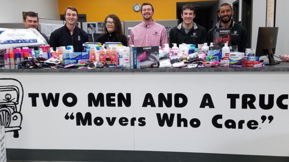 Photo of donations collected for Middle Way House. Counter is covered and there are six employees standing behind the counter.