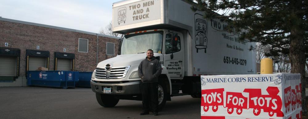 two men and a truck mover standing by truck with toys for tots box