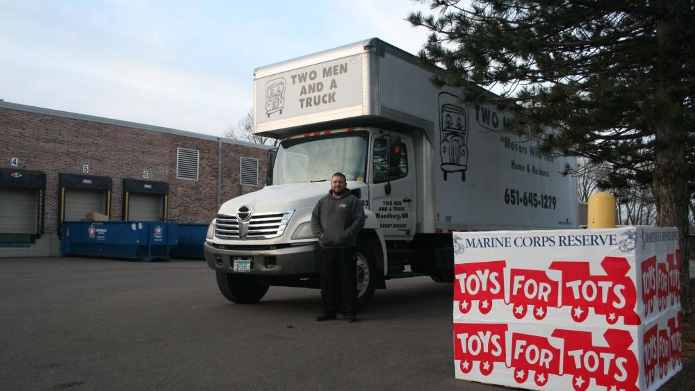 two men and a truck mover standing by truck with toys for tots box