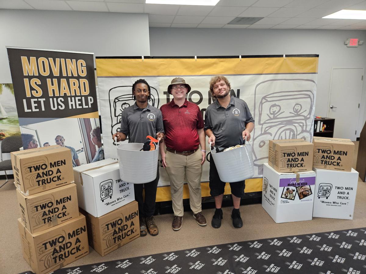 three guys holding donations with boxes of donations in front of business signs