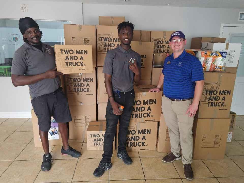 three men standing in front of a lrage stack of donation boxes in a building