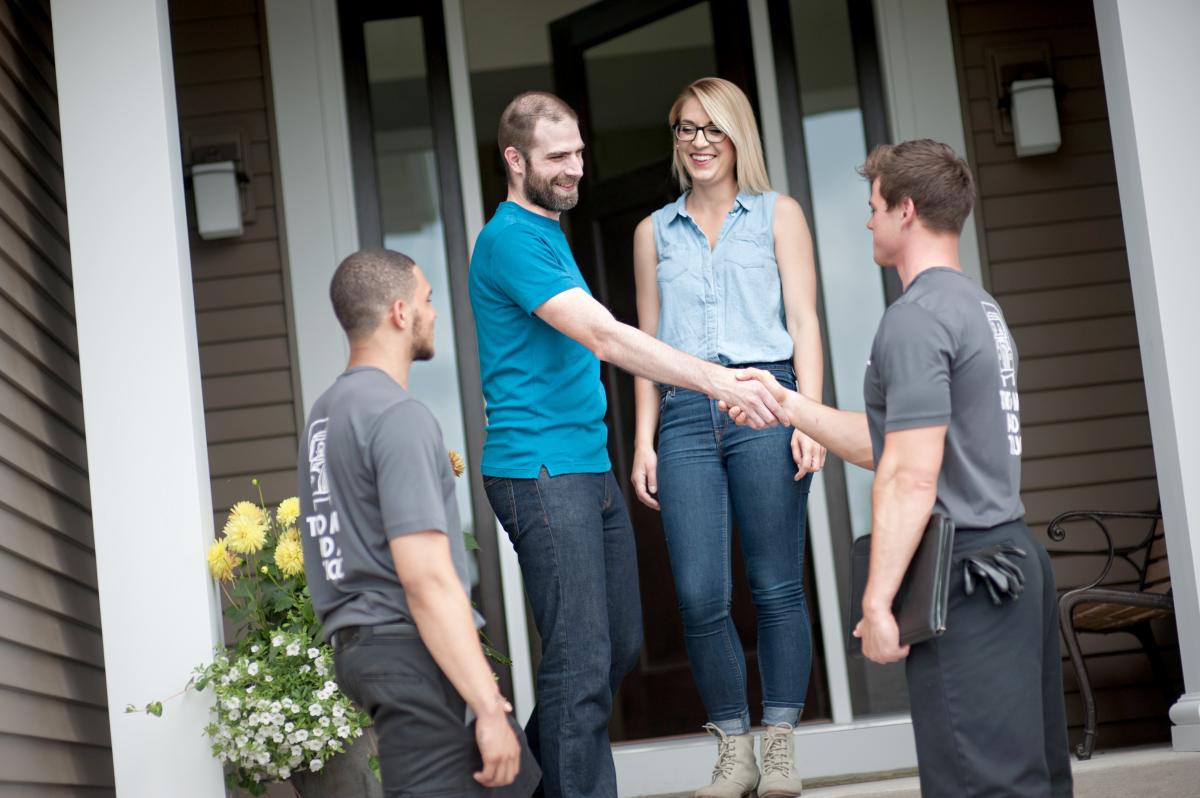 customers and two men and a truck movers standing on front porch shaking hands