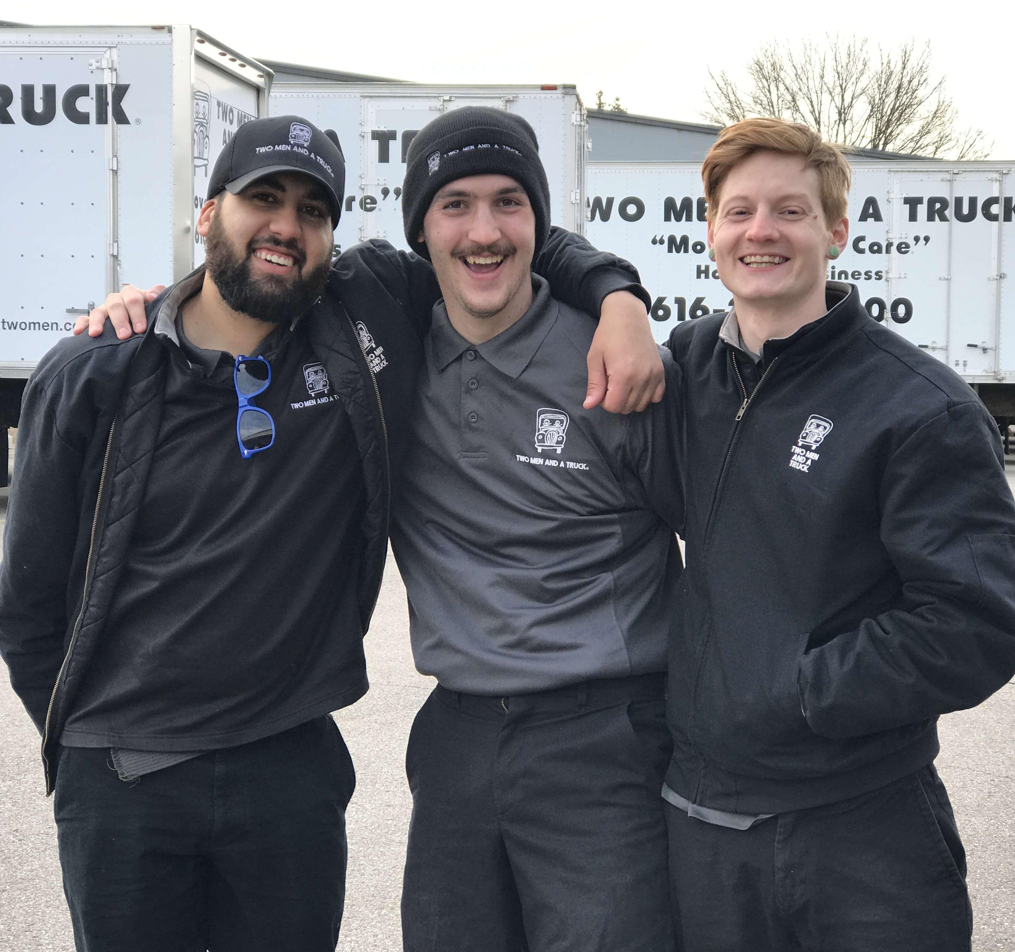 group of three movers standing in front of the trucks smiling