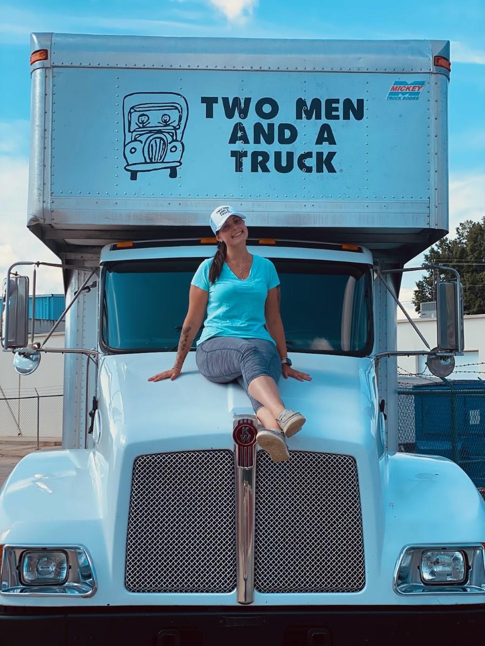 Team member Allison sitting on the hood of a moving truck