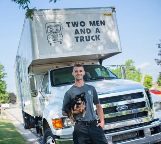 Two men and a truck mover holding a dog in front of a truck
