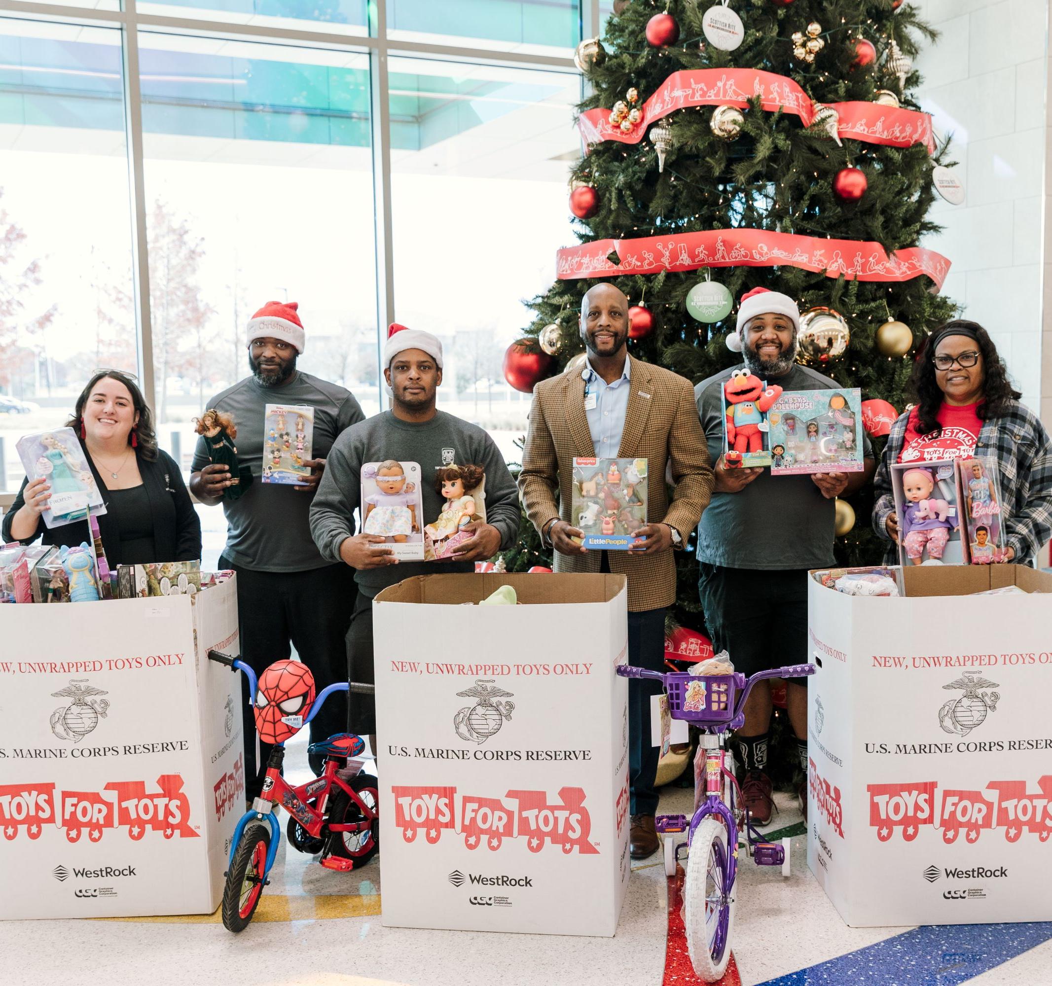 TWO MEN AND A TRUCK Dallas movers standing in front of Christmas Tree with Toys for Tots boxes filled with toys at Scottish Rite Hospital