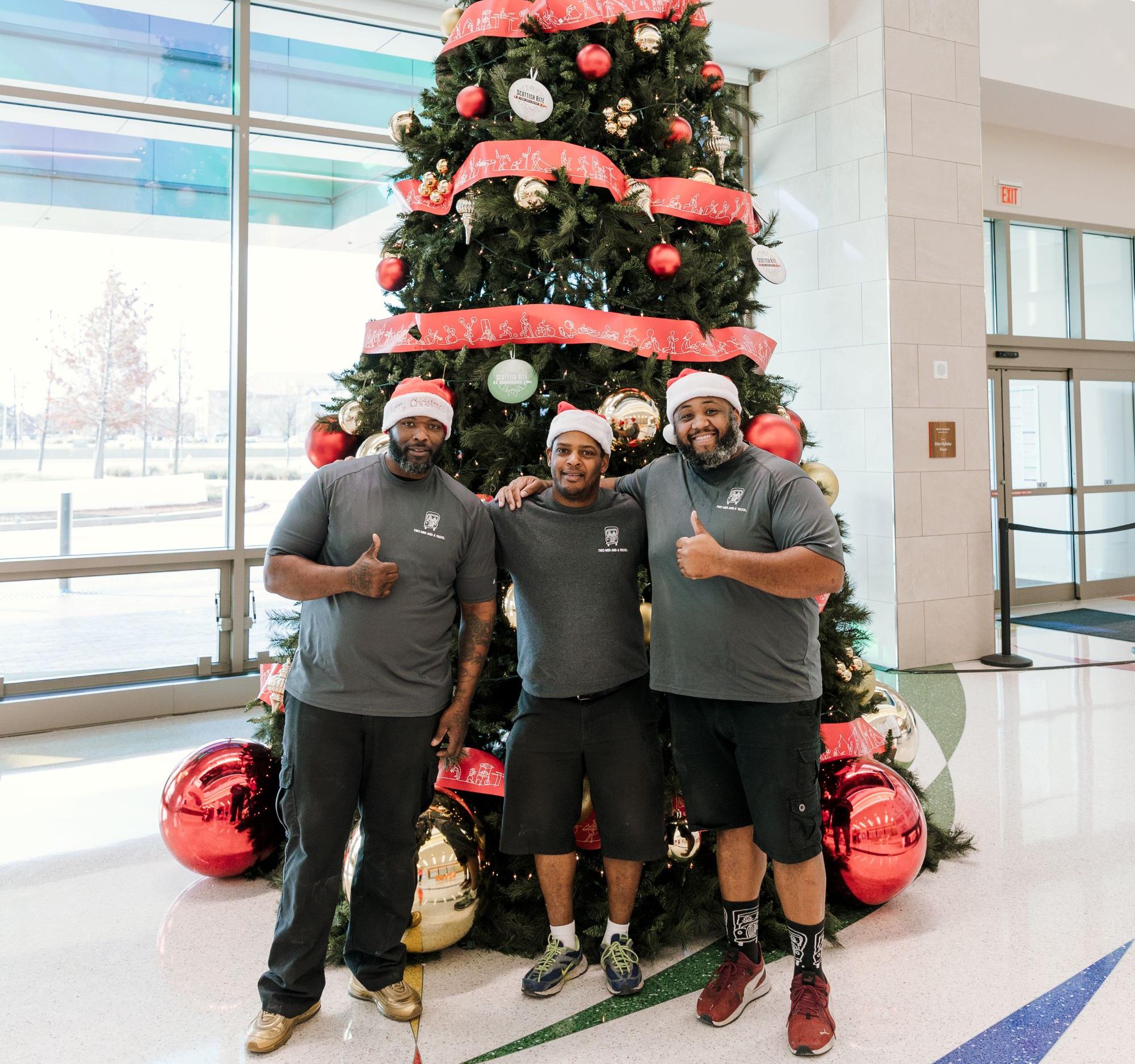  TWO MEN AND A TRUCK Dallas movers standing in front of Christmas tree wearing santa hats