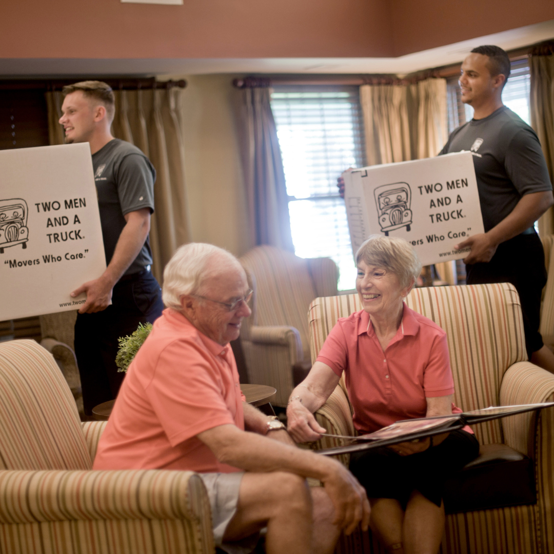 seniors sitting on chairs with movers with boxes behind them