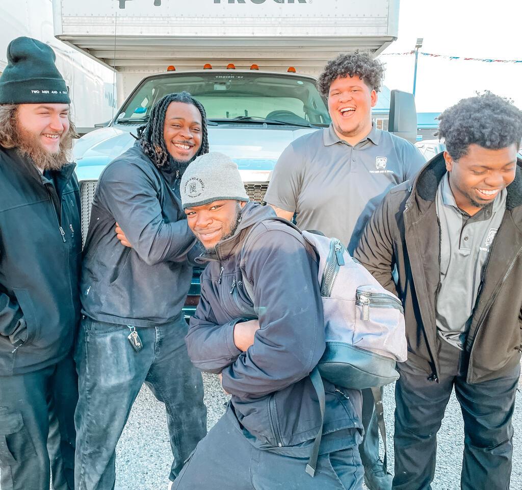 a group of movers in front of a truck smiling and laughin
