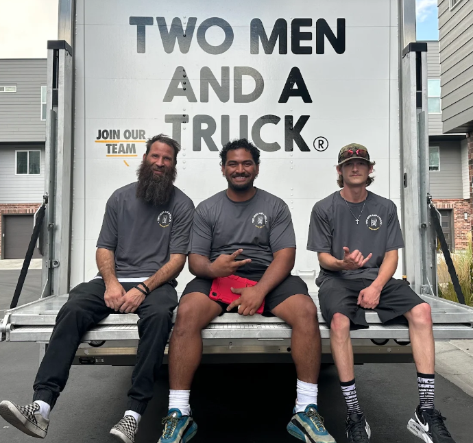 three movers are sitting on the back of a moving truck