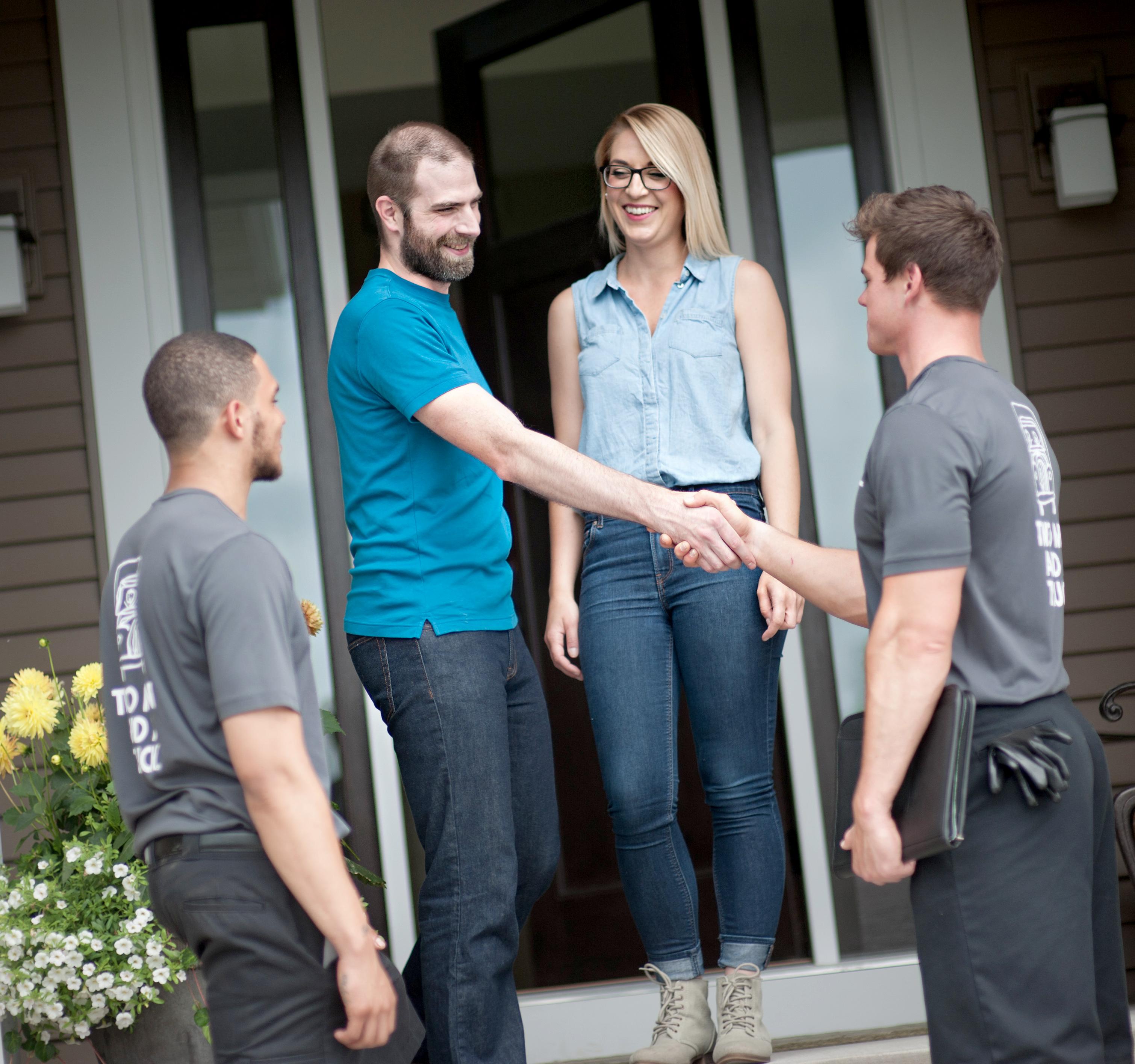 customers and two men and a truck movers standing on front porch shaking hands