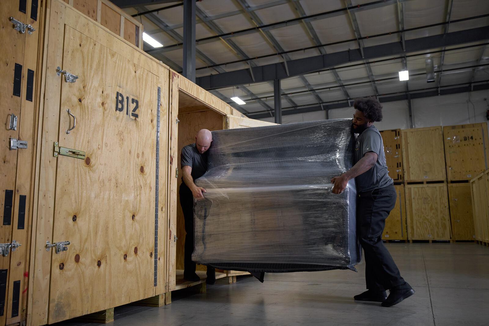 two movers are carrying a piano into a storage unit