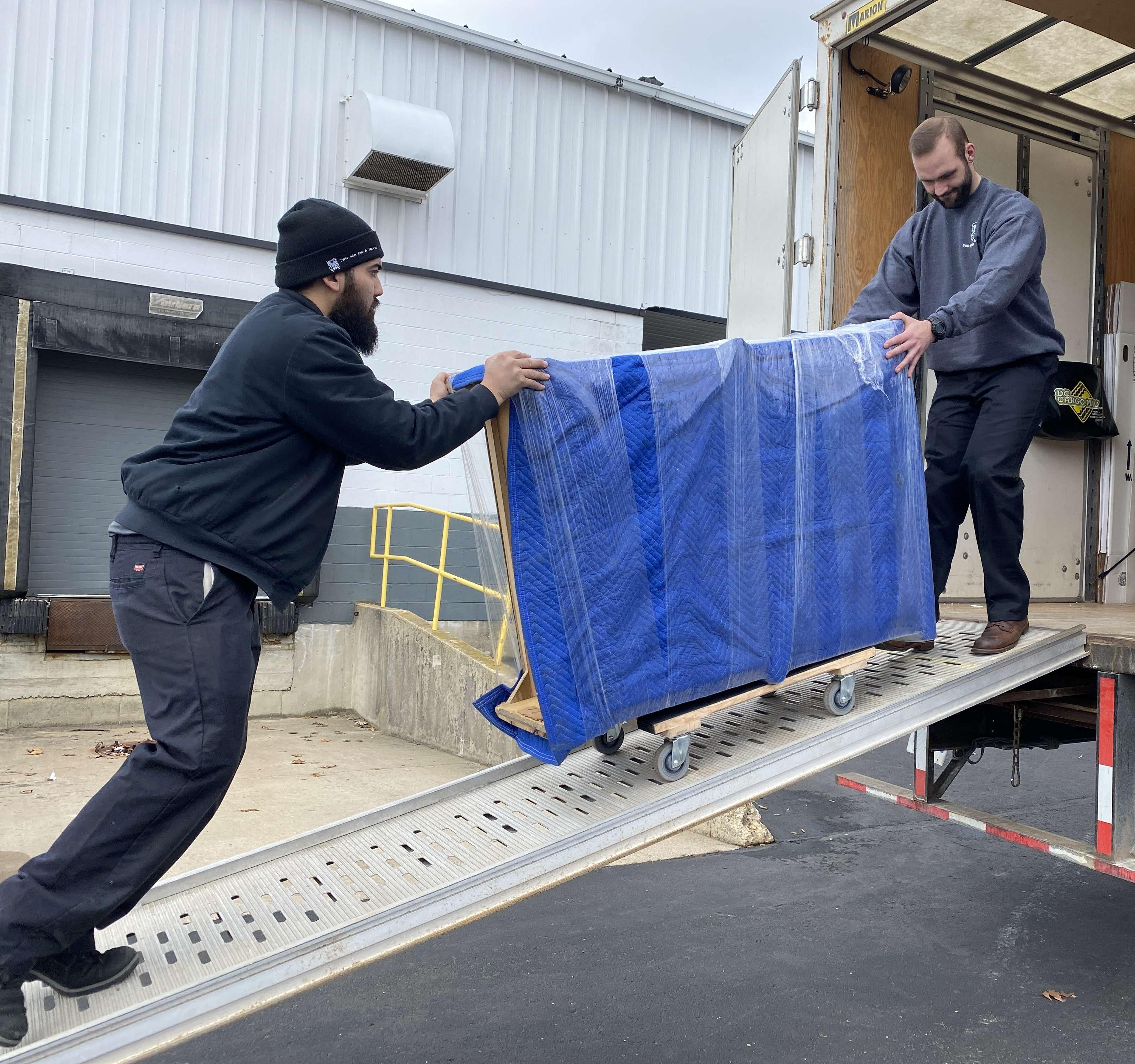 Trainer helping a trainee with a big piece of furniture up the ramp to the truck