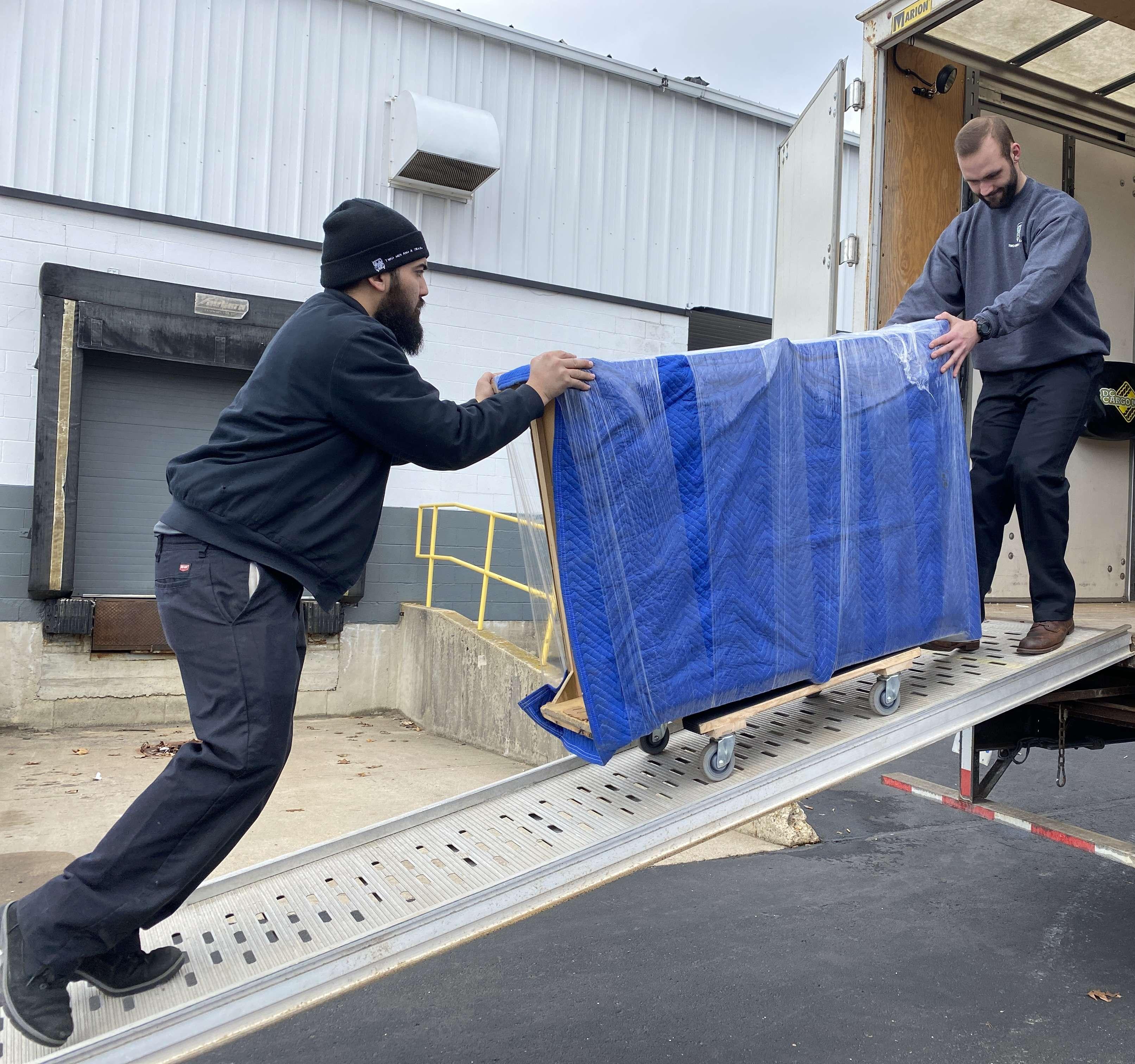 Two movers moving a pad wrapped item up the ramp of the truck