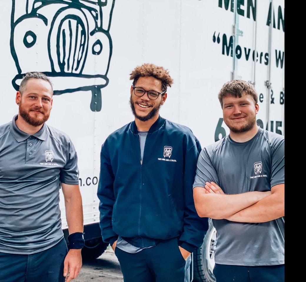 Three movers standing in front of a moving truck smiling