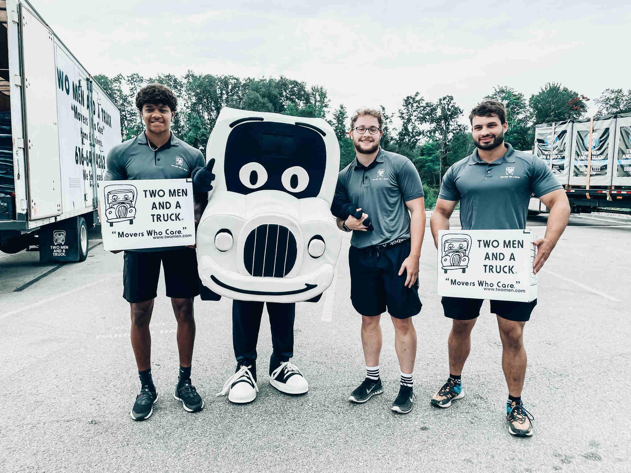 three movers holding boxes and standing with the truckie mascot