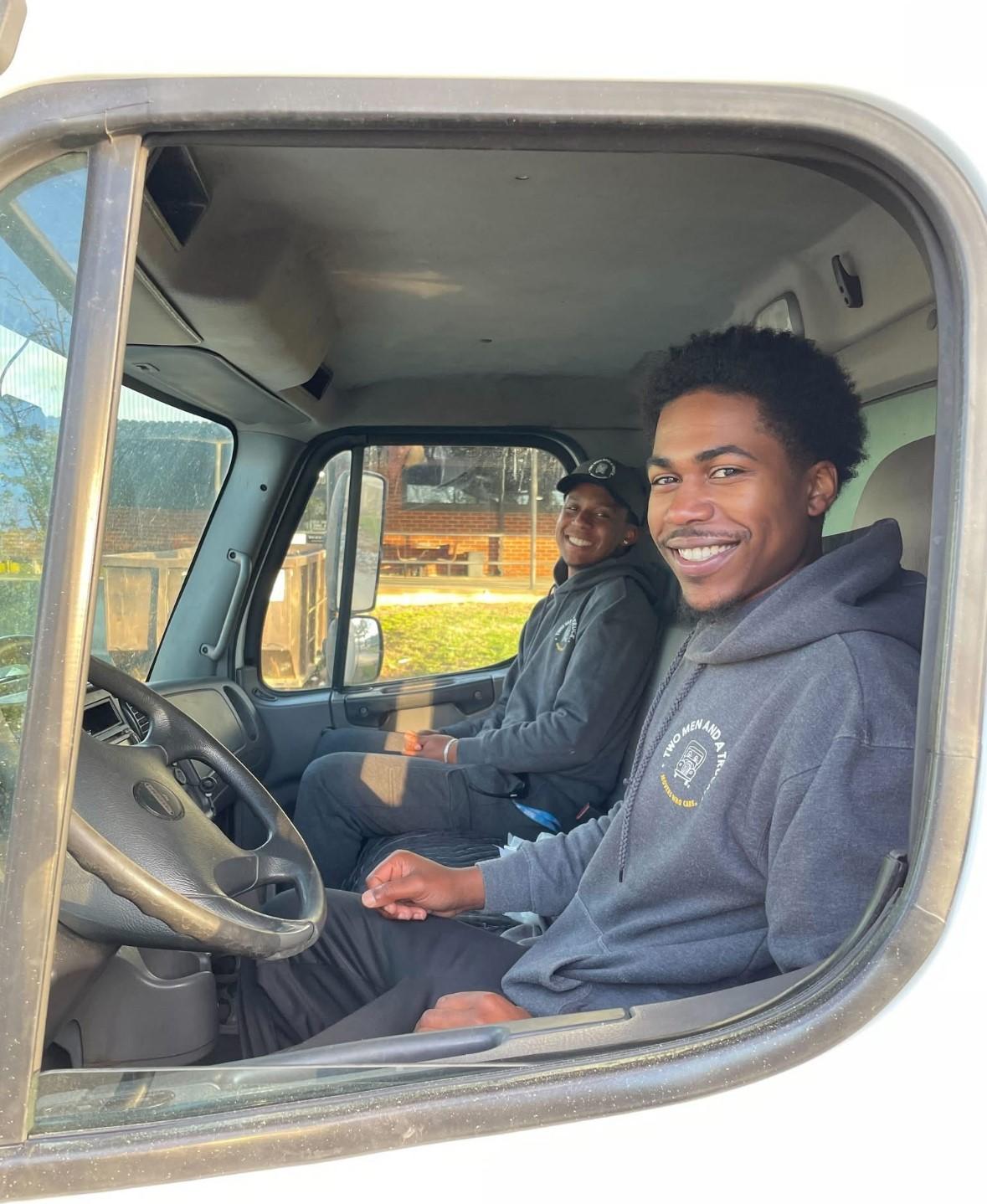 2 movers in the cab of a truck with big smiles