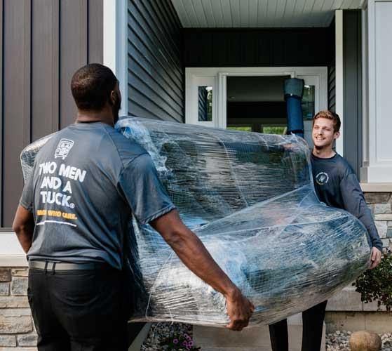 two movers carrying a couch towards an open door