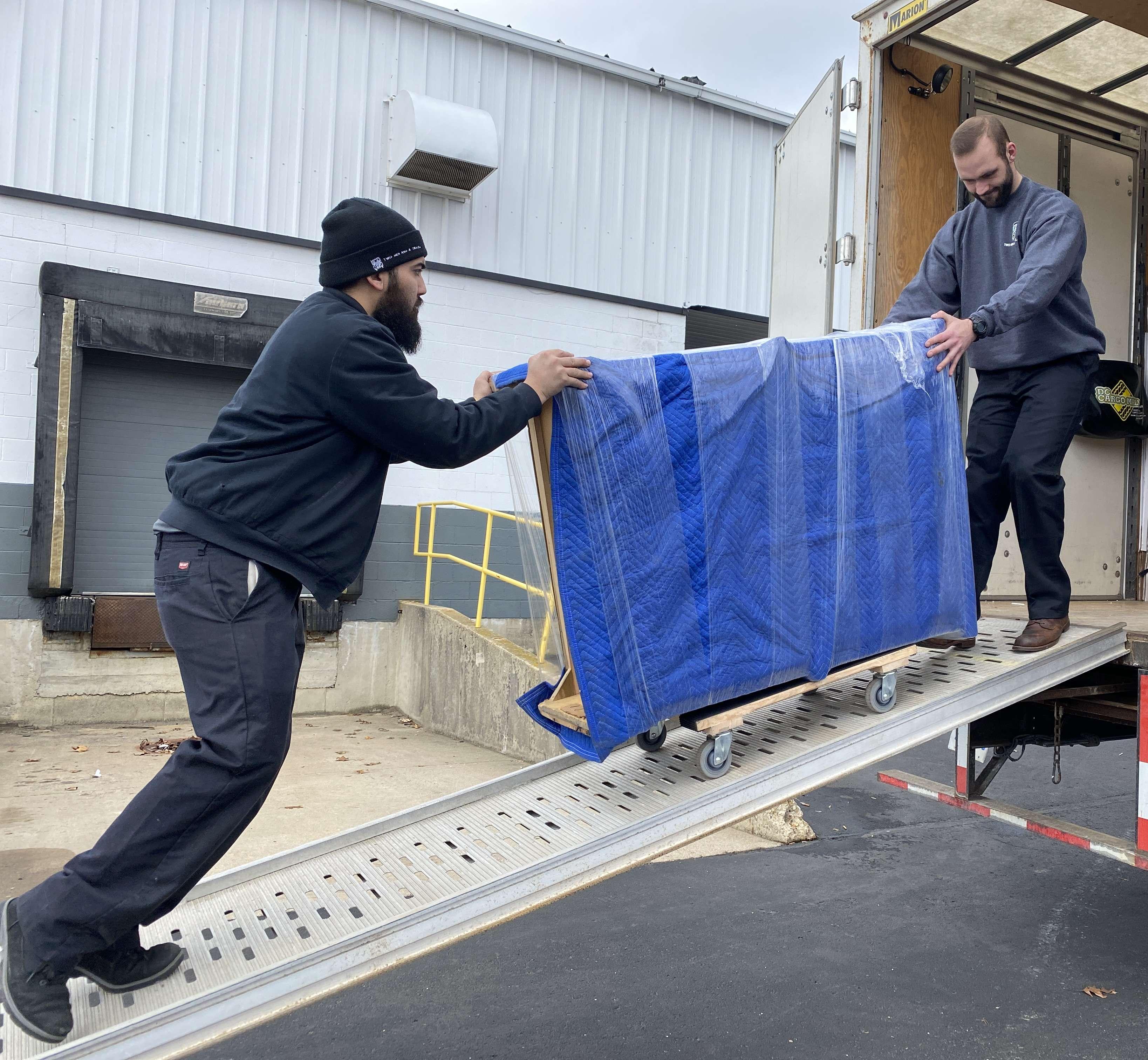 Two movers moving a pad wrapped item up the ramp of the truck