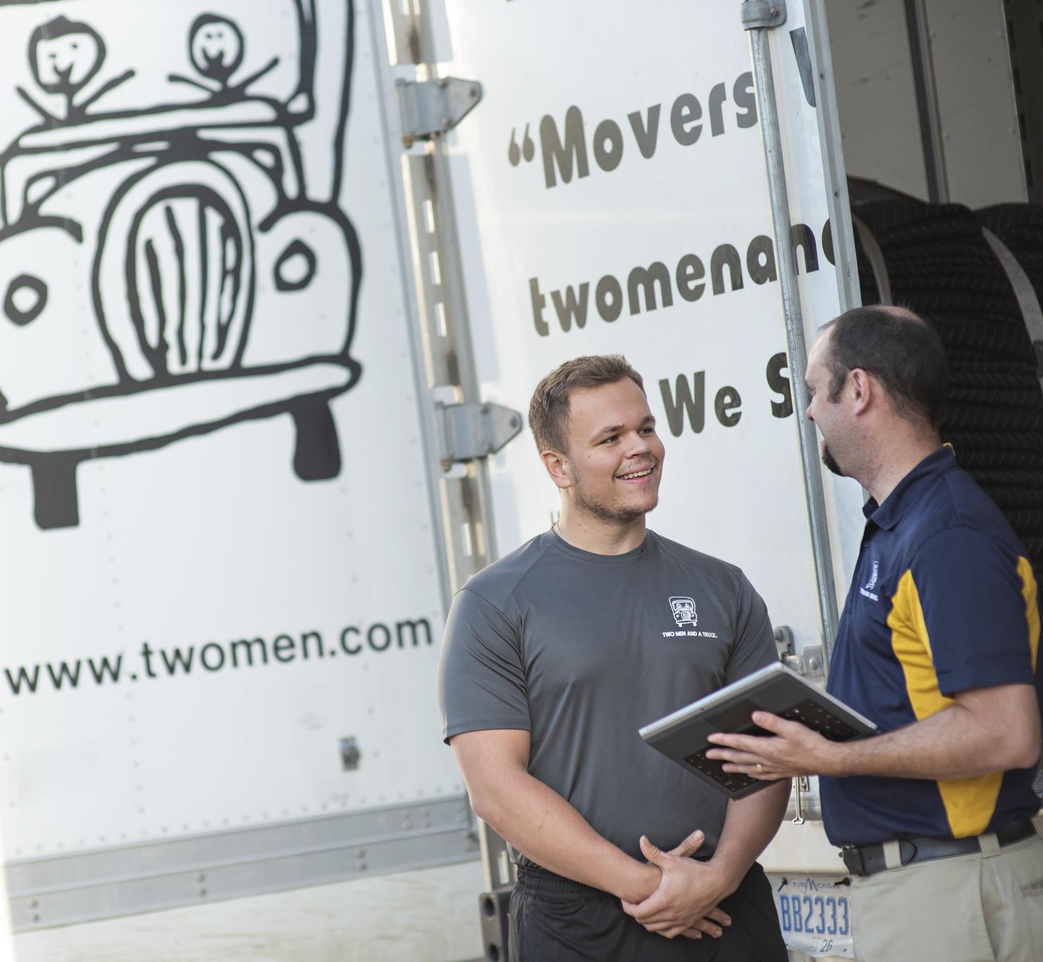 Two men standing beside a moving truck talking