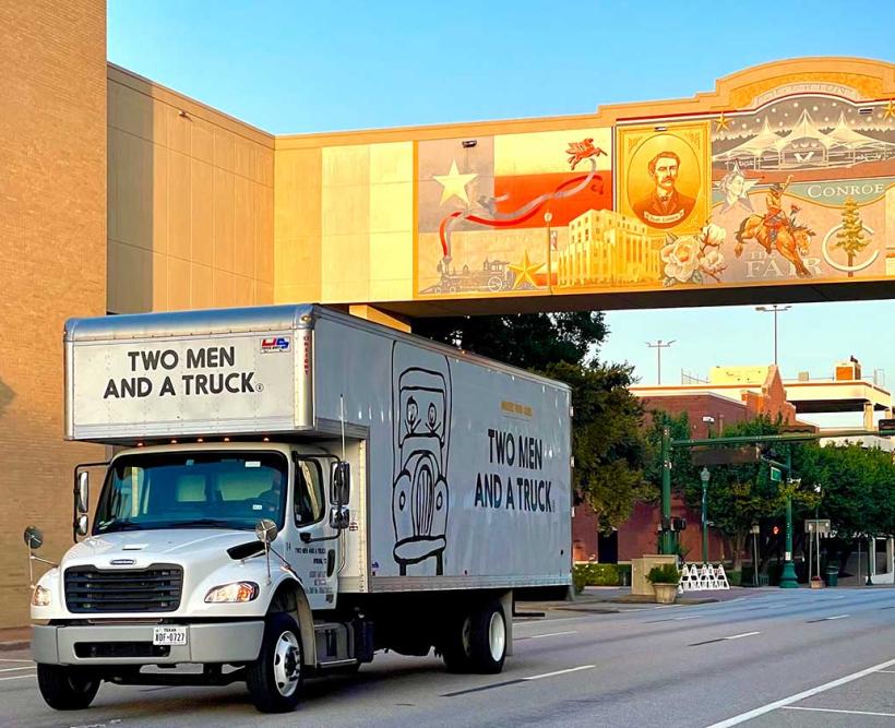 Moving truck driving under Conroe city sign
