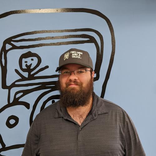 ozzie is wearing a gray two men and a truck hat standing in front of a blue wall with the two men and a truck logo on it