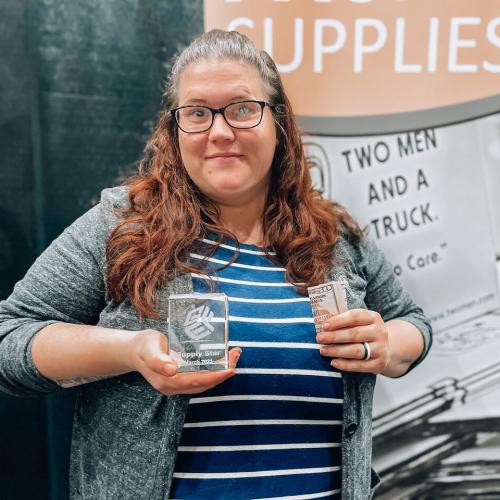 Kristie is standing in front of a marketing sign holding a trohpy
