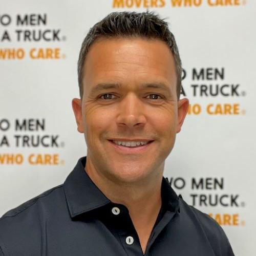 Bob wearing a black polo standing in front of two men and a truck backdrop