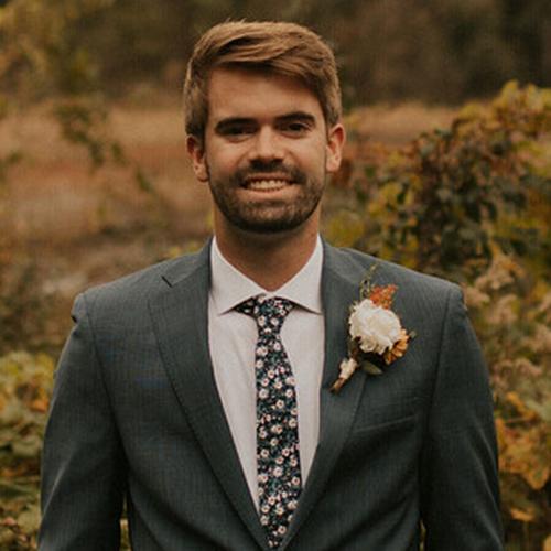 jared is in a suit standing in front of fall foliage