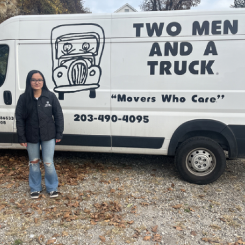 smiling woman standing in front of a two men and a truck moving van