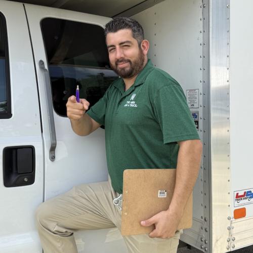 Operations manager standing in front of moving truck with clipboard 