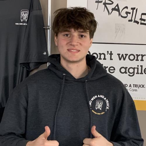man in a black hoodie smiling, giving two thumbs up 